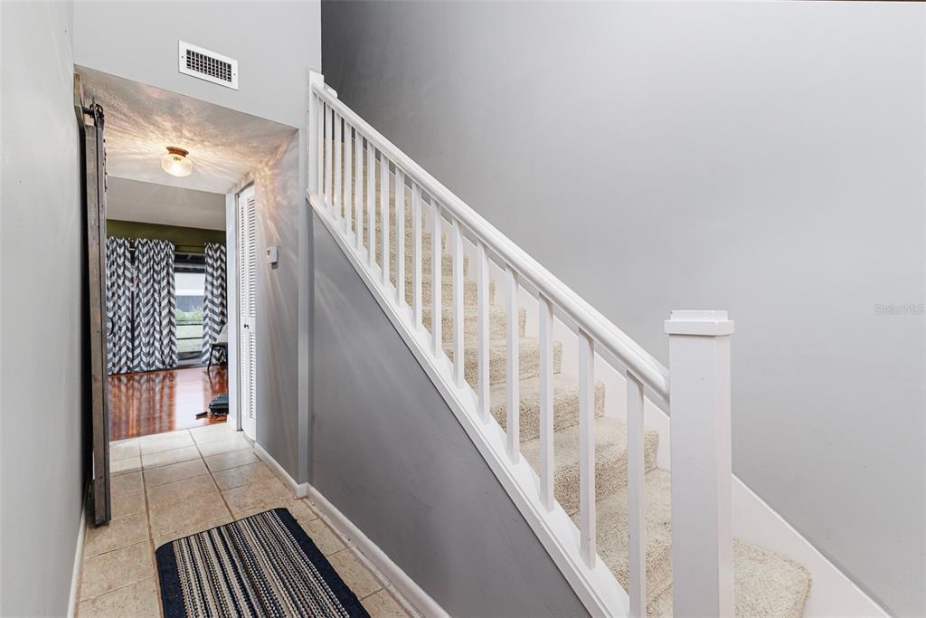 A carpeted staircase with a white railing sits beside a tiled hallway leading to a room — 2500 21ST STREET NW UNIT 23, WINTER HAVEN, FL