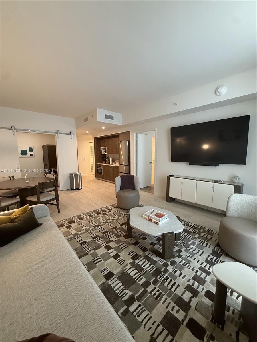 A modern living room features a large television, patterned area rug, and an open kitchen — 1611 SW 2nd Avenue # 202, Miami FL 33129, MIAMI, FL