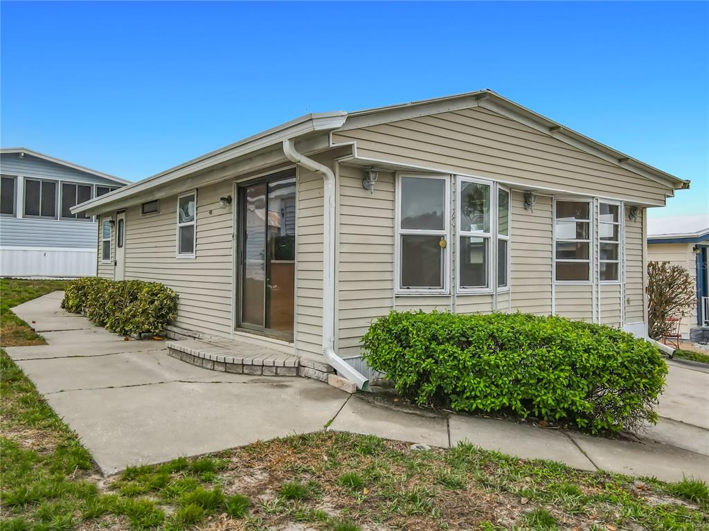 A beige mobile home with vinyl siding, a sliding glass door, and a concrete walkway — 9705 LAKE BESS ROAD UNIT 715, WINTER HAVEN, FL