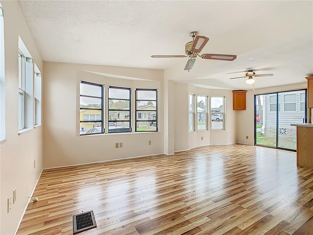 An empty living area features wood-look flooring, two ceiling fans, and multiple windows — 9705 LAKE BESS ROAD UNIT 715, WINTER HAVEN, FL