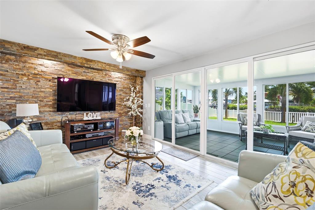 A living room features a stone accent wall, a television, and sliding glass doors to a patio — 485 FLAMINGO DRIVE, APOLLO BEACH, FL