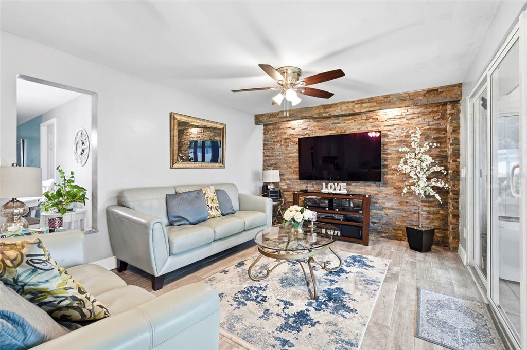 A living room features a stone accent wall, a television, and two light-colored sofas — 485 FLAMINGO DRIVE, APOLLO BEACH, FL