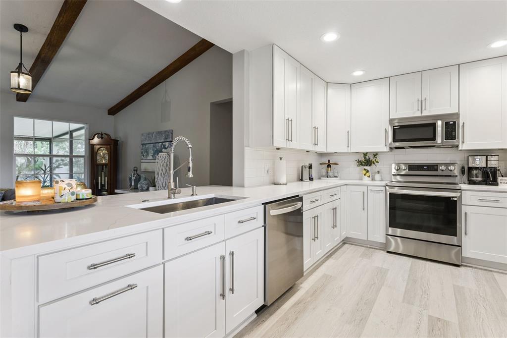 A modern kitchen features white cabinets, stainless steel appliances, and a quartz countertop island — 1708 CREOLE COURT, ORLANDO, FL