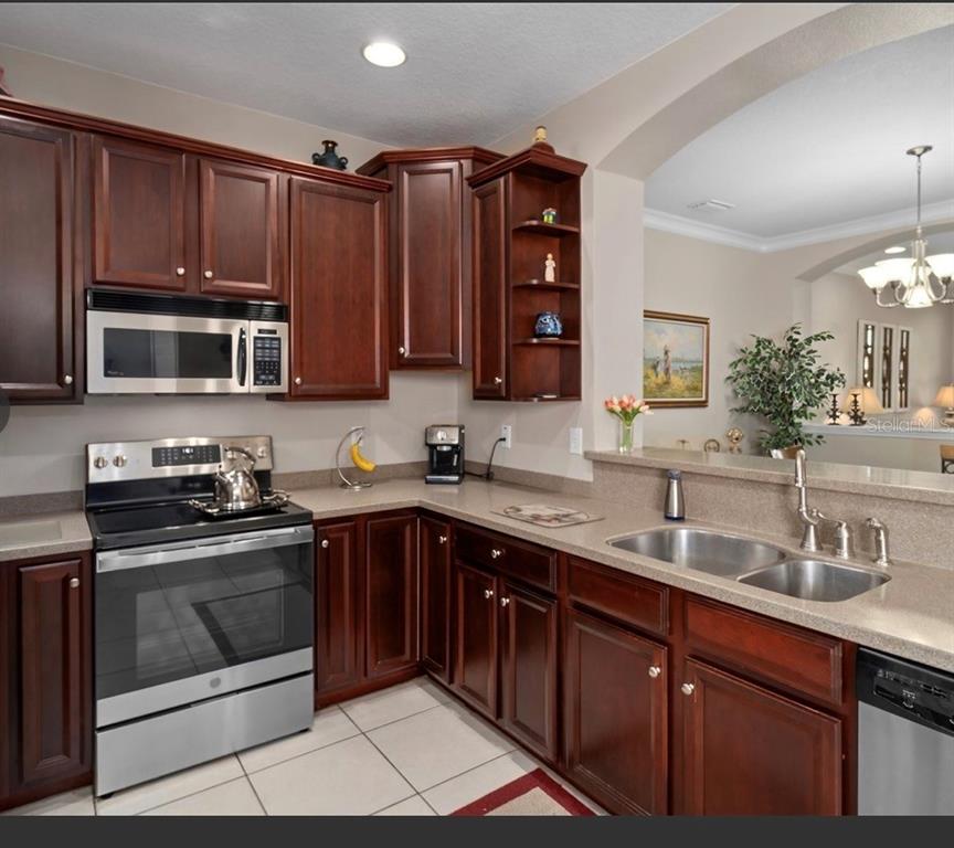 A kitchen features dark wood cabinets, stainless steel appliances, and a beige countertop — 10409 CRIMSON PARK LANE UNIT 105, TAMPA, FL