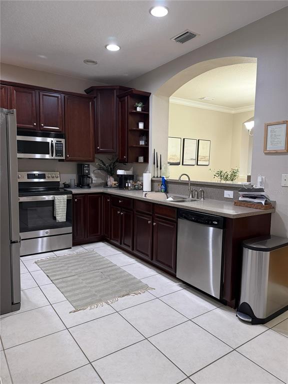 A kitchen features dark wood cabinets, stainless steel appliances, and a light-colored tile floor — 10409 CRIMSON PARK LANE UNIT 105, TAMPA, FL