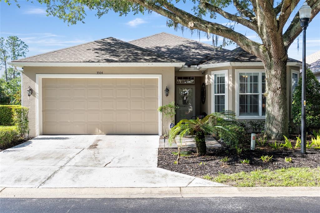A single-story house with a beige stucco exterior, a two-car garage, and a large tree — 3304 SW 38TH STREET, OCALA, FL