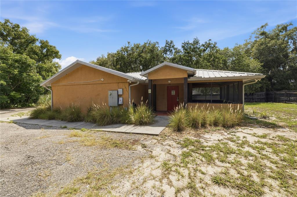 A single-story house with a tan stucco exterior, a metal roof, and a screened porch — 2250 N VOLUSIA AVENUE, ORANGE CITY, FL