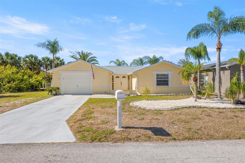 A yellow single-story house with a white garage door, concrete driveway, and palm trees — 7418 ISLANDER LANE, HUDSON, FL