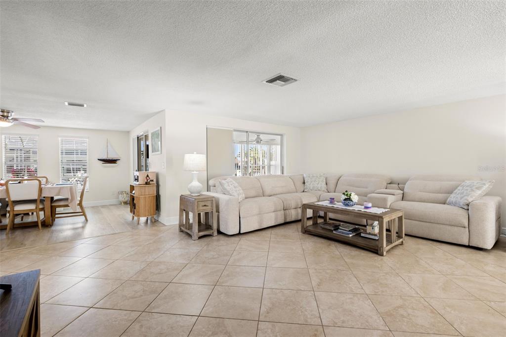 A living room with beige tile floors, a large sectional sofa, and an adjacent dining area — 7418 ISLANDER LANE, HUDSON, FL