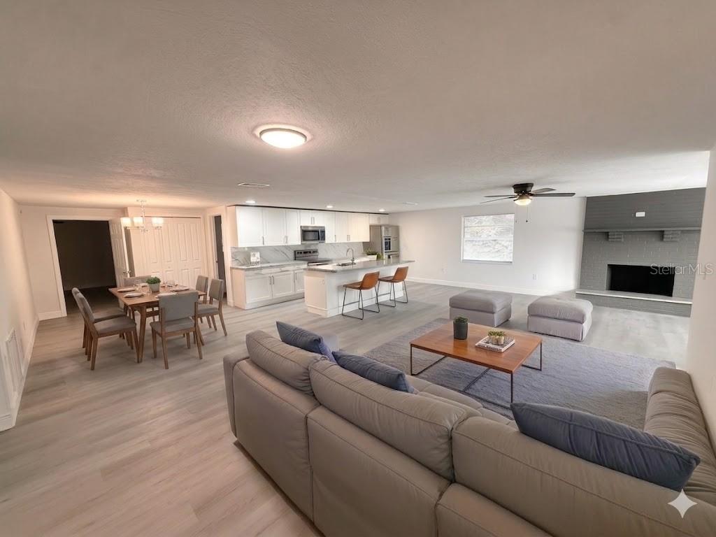 An open-concept living room, dining area, and kitchen with light wood floors and a fireplace — 1251 NW 23RD AVENUE, OCALA, FL