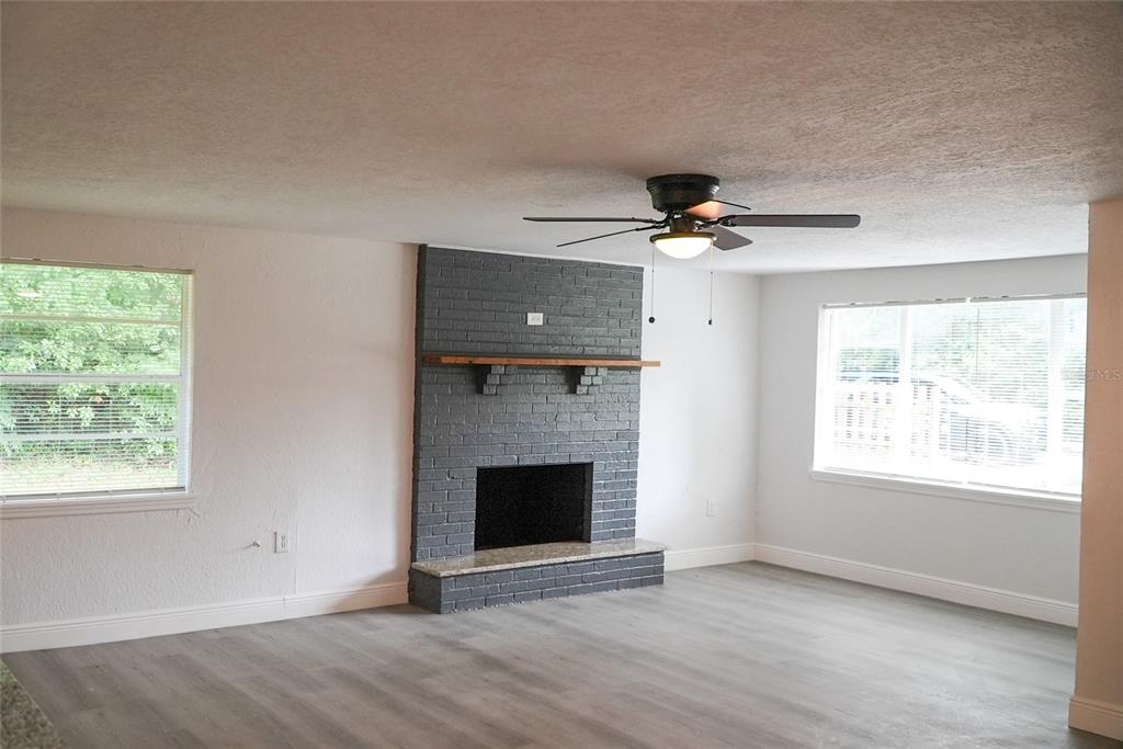 A living room features gray wood-look flooring, white walls, and a gray painted brick fireplace — 1251 NW 23RD AVENUE, OCALA, FL