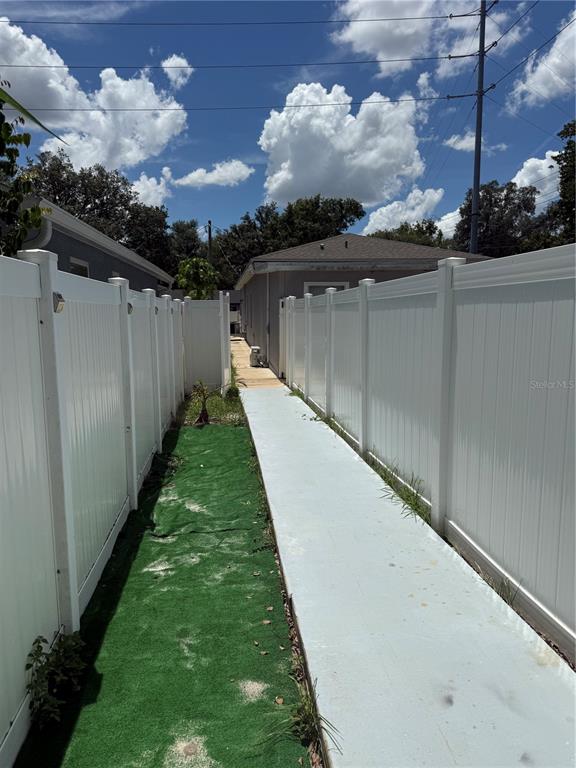 A narrow walkway with a concrete path and artificial turf sits between two white fences — 1923 W SKAGWAY AVENUE, TAMPA, FL