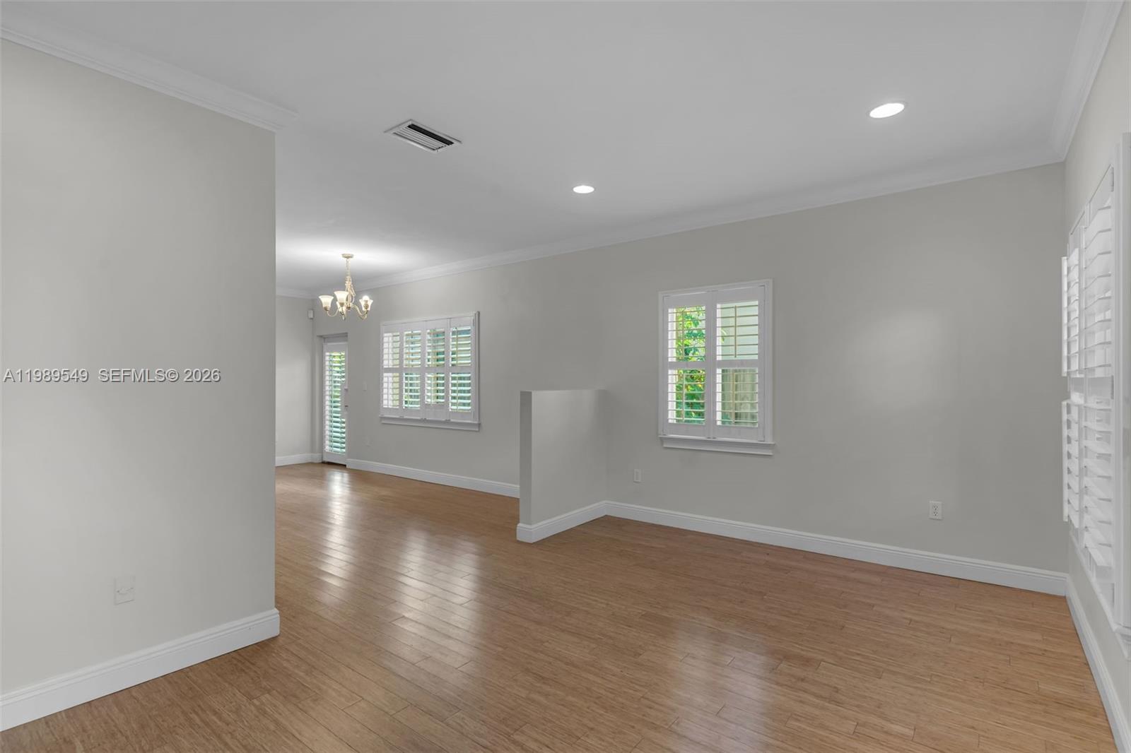 An empty room with light wood flooring, white walls, and plantation shutters on the windows — 7048 SW 83rd Ct, Miami FL 33143, MIAMI, FL