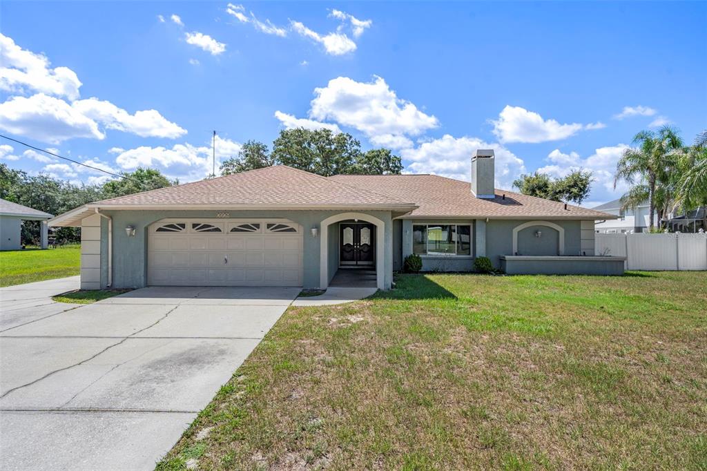 A single-story house with a two-car garage, light green stucco siding, and a chimney — 7376 SKYLARK DRIVE, SPRING HILL, FL