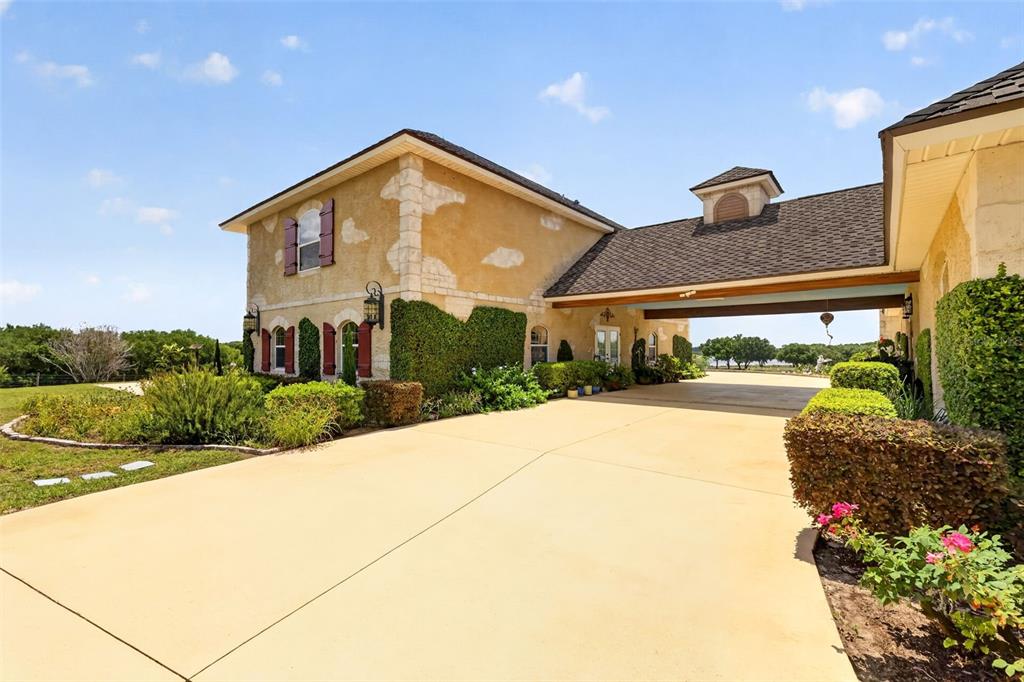 A tan stucco house with stone accents features a large driveway and a covered porte-cochère — 17269 SE 260TH AVENUE ROAD, UMATILLA, FL