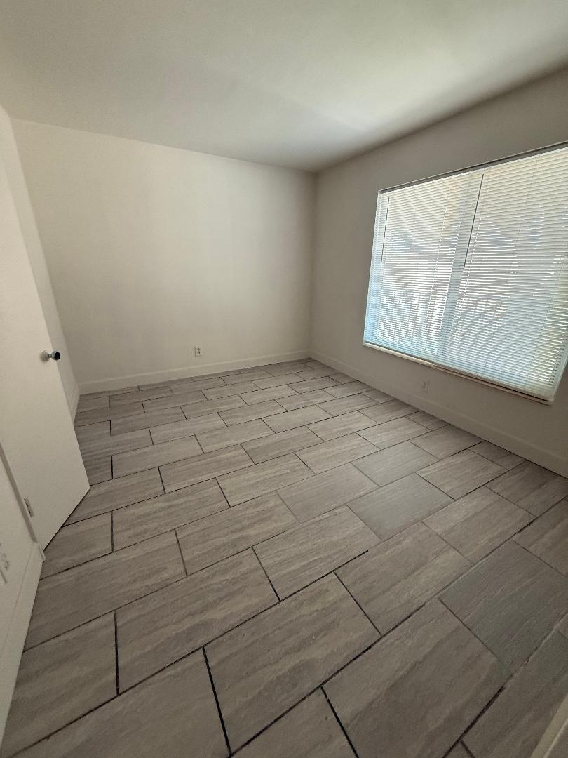 An empty room with light gray wood-look tile flooring and a large window with blinds — 2317 NE 2nd Street # 5, Pompano Beach FL 33062, POMPANO BEACH, FL