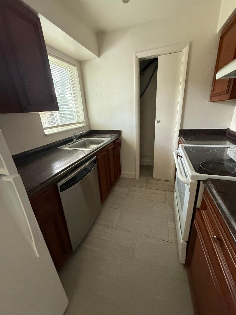 A galley-style kitchen features dark wood cabinets, dark countertops, stainless steel appliances, and tile flooring — 2317 NE 2nd Street # 5, Pompano Beach FL 33062, POMPANO BEACH, FL