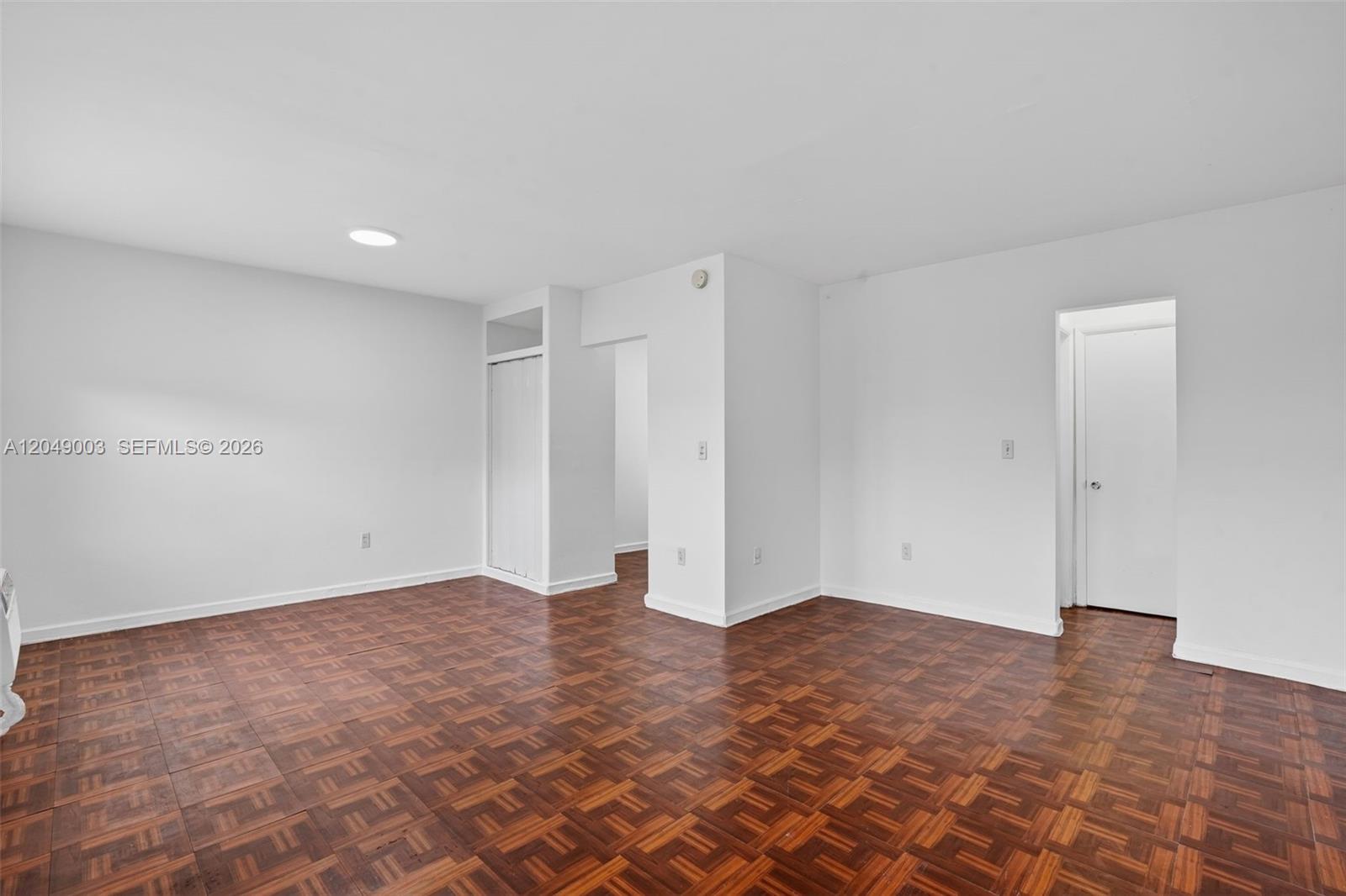 An empty room features white walls, a white door, and dark parquet wood flooring — 2170 NW Flagler Ter, Miami FL 33125, MIAMI, FL
