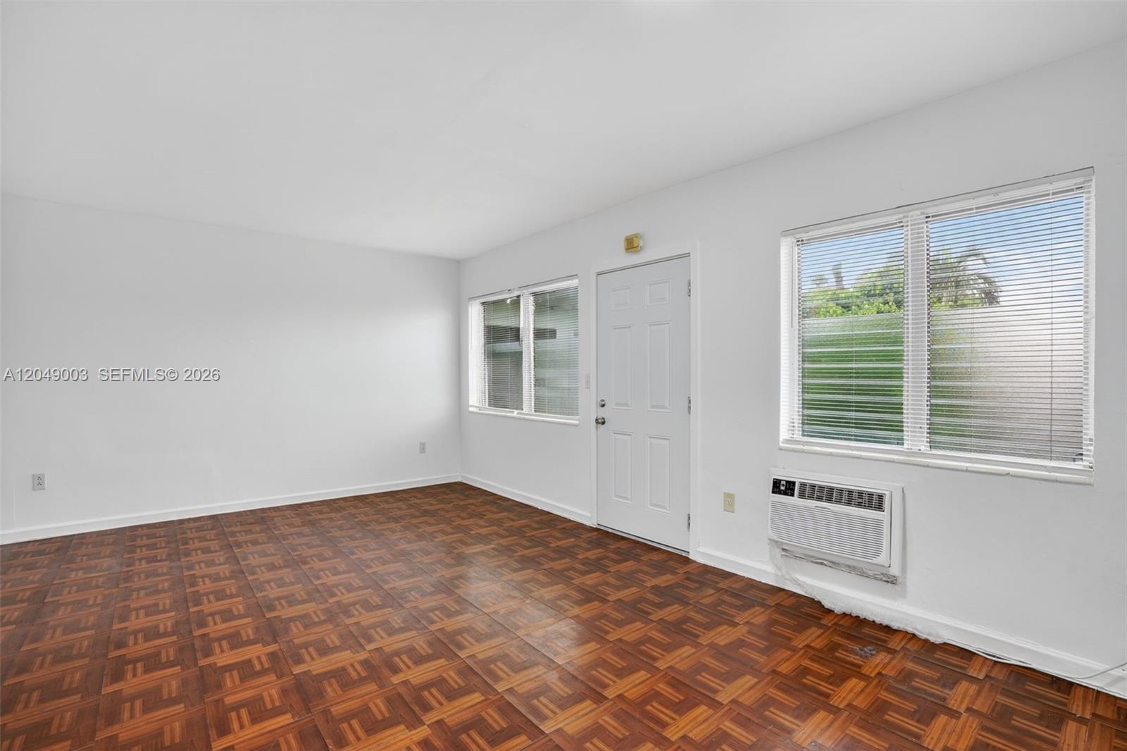 An empty room features white walls, parquet wood flooring, a window, and a door — 2170 NW Flagler Ter, Miami FL 33125, MIAMI, FL