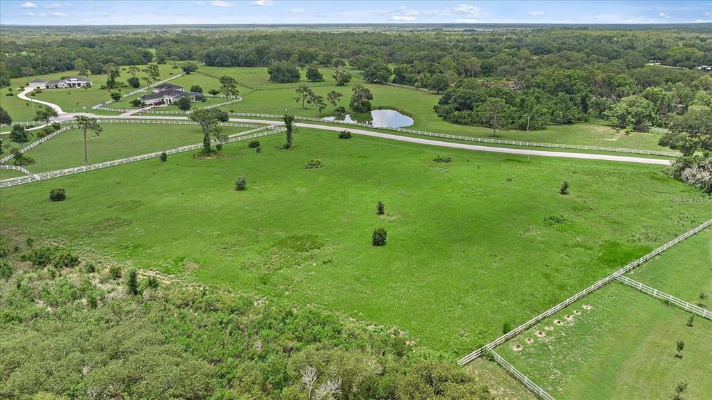 An aerial view shows a large, grassy pasture with white fencing and a small pond — 15945 PAINTED POST LANE, SARASOTA, FL