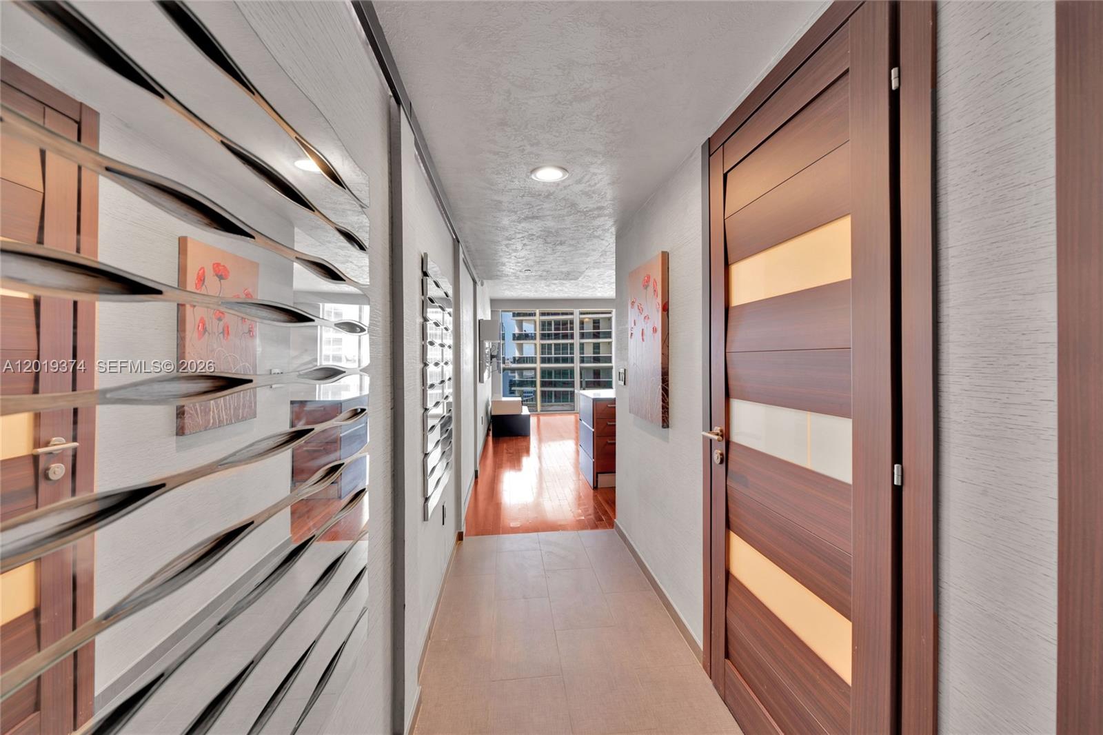 A hallway with tile flooring leads toward a living area with hardwood floors and windows — 1830 S Ocean Dr # 2705, Hallandale Beach FL 33009, HALLANDALE BEACH, FL
