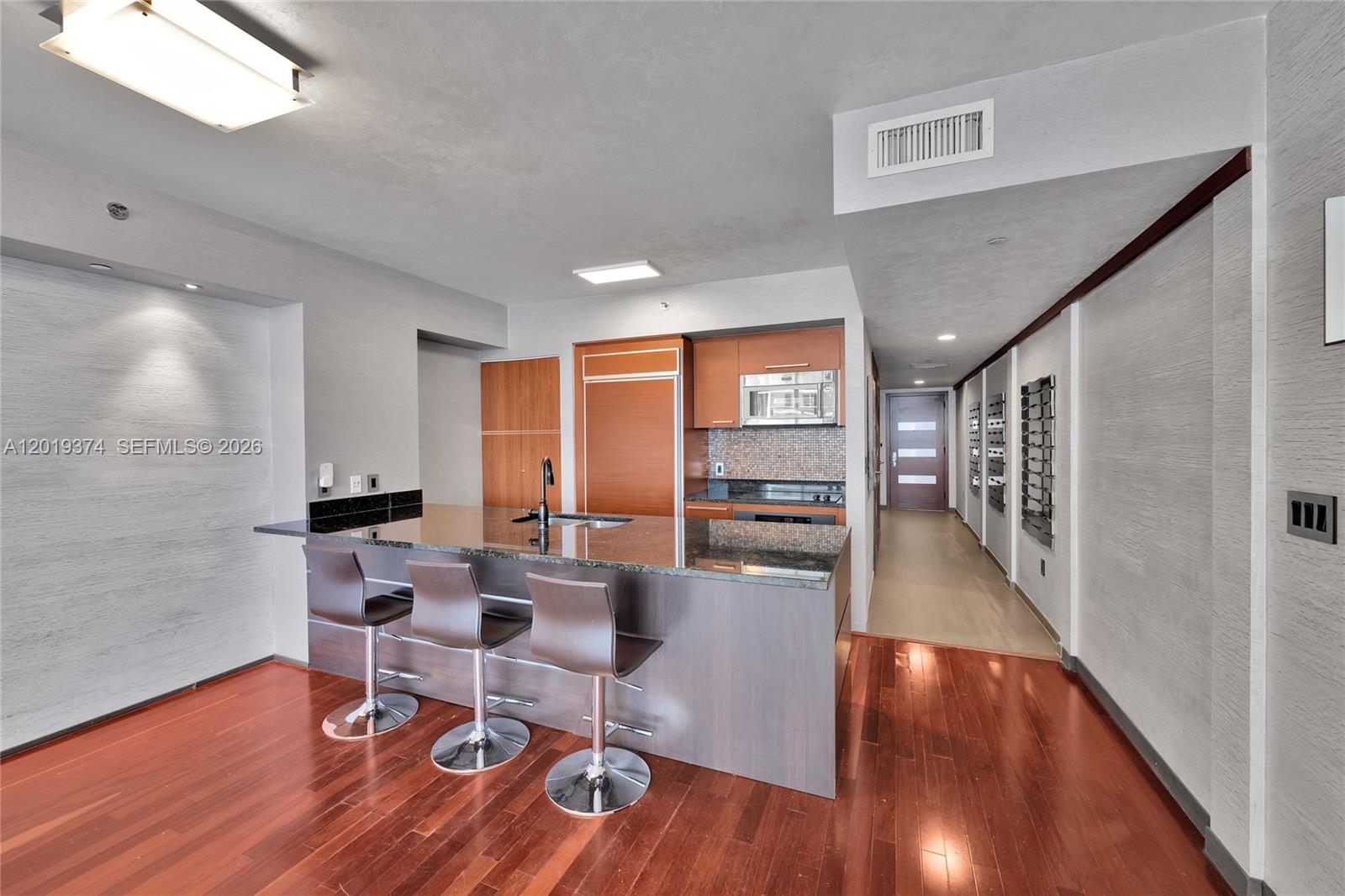 A modern kitchen features a dark granite island with three stools and wood cabinetry — 1830 S Ocean Dr # 2705, Hallandale Beach FL 33009, HALLANDALE BEACH, FL