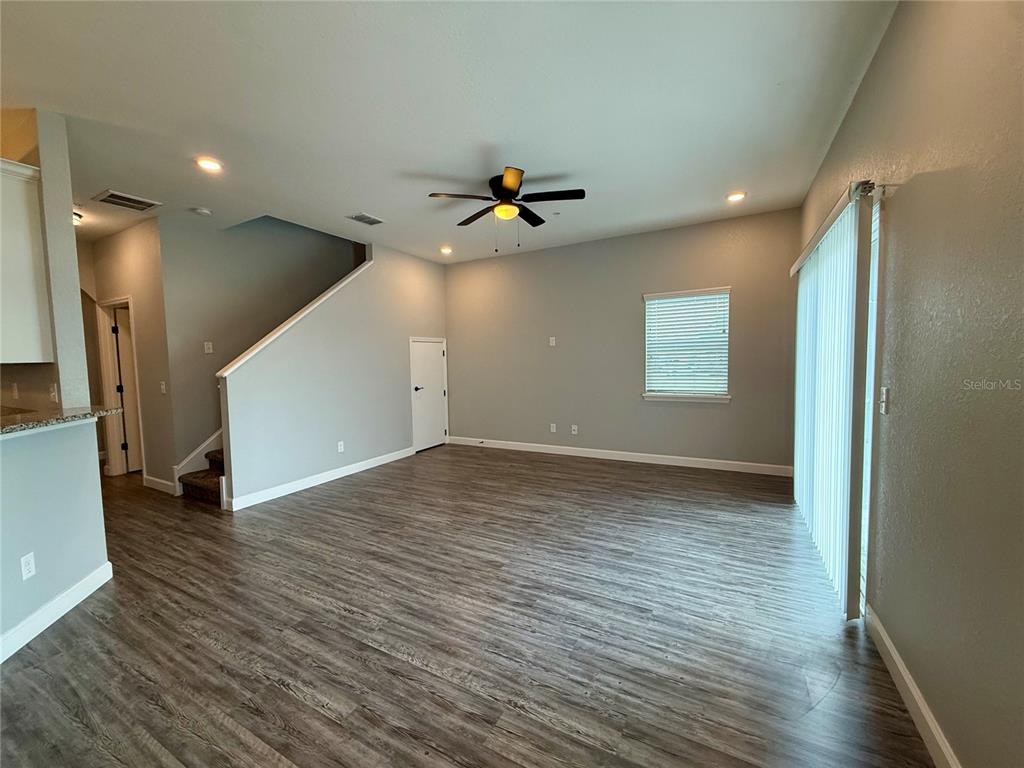 An open-concept living room features gray walls, wood-look flooring, a ceiling fan, and stairs — 2608 TANOAK TERRACE, WINTER HAVEN, FL