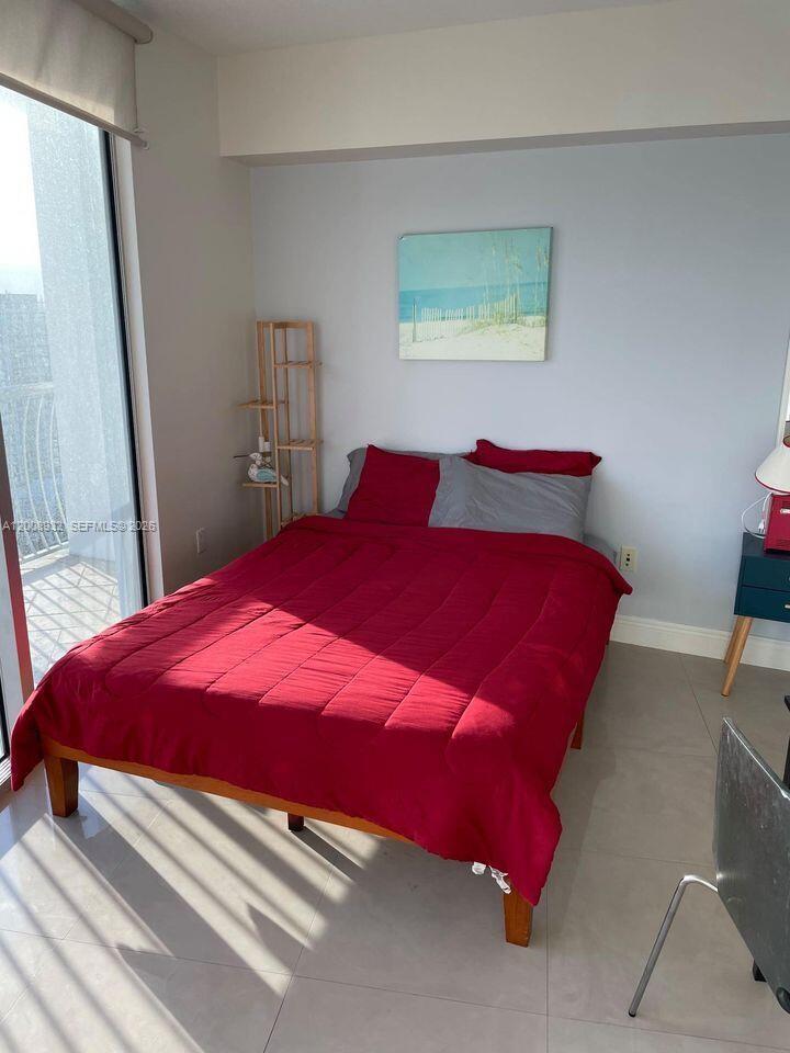 A bedroom features a bed with a red comforter, a wooden shelf, and a balcony door — 1750 N Bayshore Dr # 2514, Miami FL 33132, MIAMI, FL