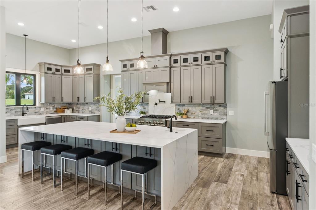 A modern kitchen features gray cabinetry, a large white waterfall island, and wood-look tile flooring — 4050 PALMA CEIA CIRCLE, WINTER HAVEN, FL