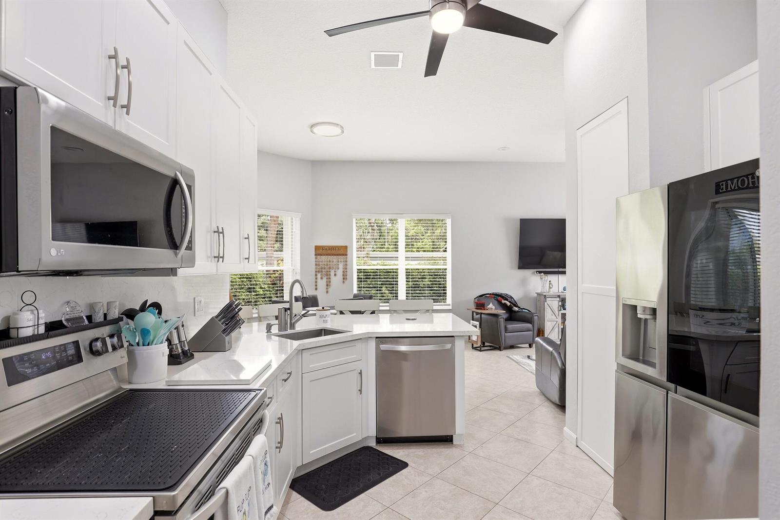 A modern kitchen with white cabinets and stainless steel appliances opens into a living area — 6583 Piemonte Drive, Boynton Beach FL 33472, BOYNTON BEACH, FL