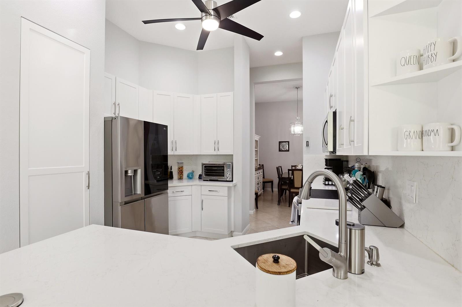 A white kitchen features stainless steel appliances, quartz countertops, and an island with a sink — 6583 Piemonte Drive, Boynton Beach FL 33472, BOYNTON BEACH, FL