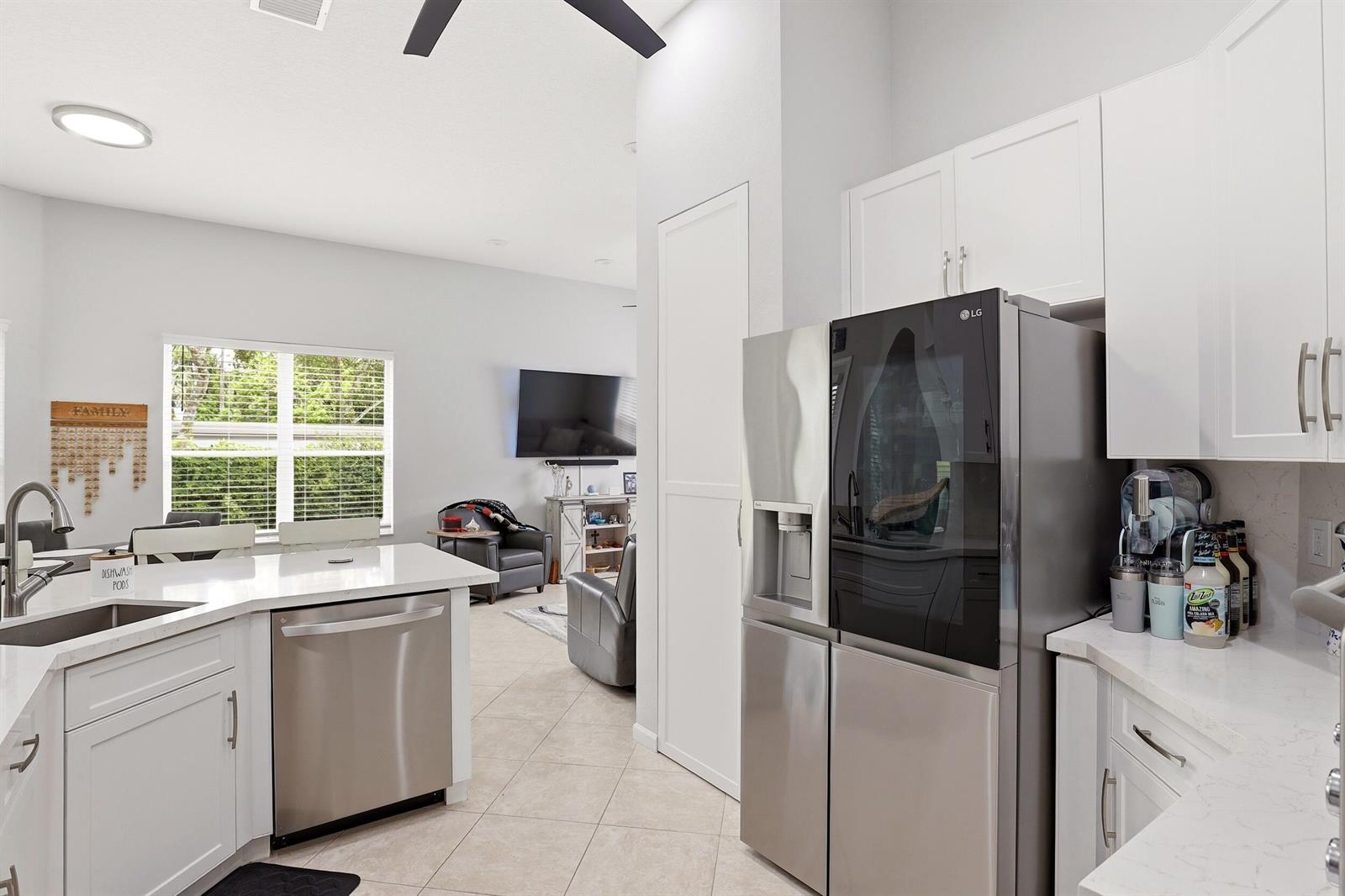A modern kitchen features white cabinets, stainless steel appliances, and a view into the living room — 6583 Piemonte Drive, Boynton Beach FL 33472, BOYNTON BEACH, FL