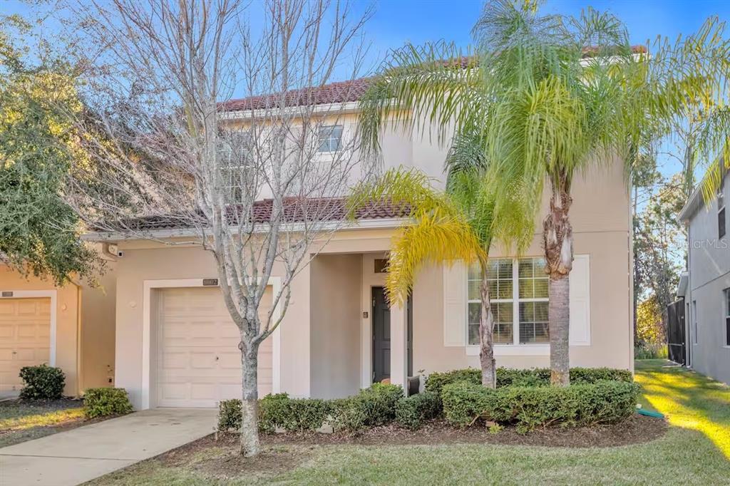 A two-story beige house with a tile roof, a single-car garage, and a palm tree — 8802 BAMBOO PALM COURT, KISSIMMEE, FL