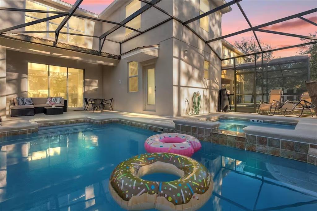 A swimming pool with two donut-shaped floats sits inside a screened-in patio area — 8802 BAMBOO PALM COURT, KISSIMMEE, FL