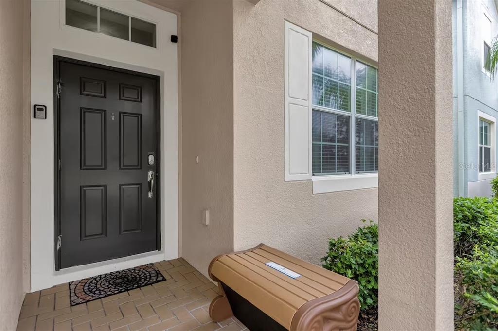 A dark front door with a transom window sits beside a bench on a porch — 8802 BAMBOO PALM COURT, KISSIMMEE, FL