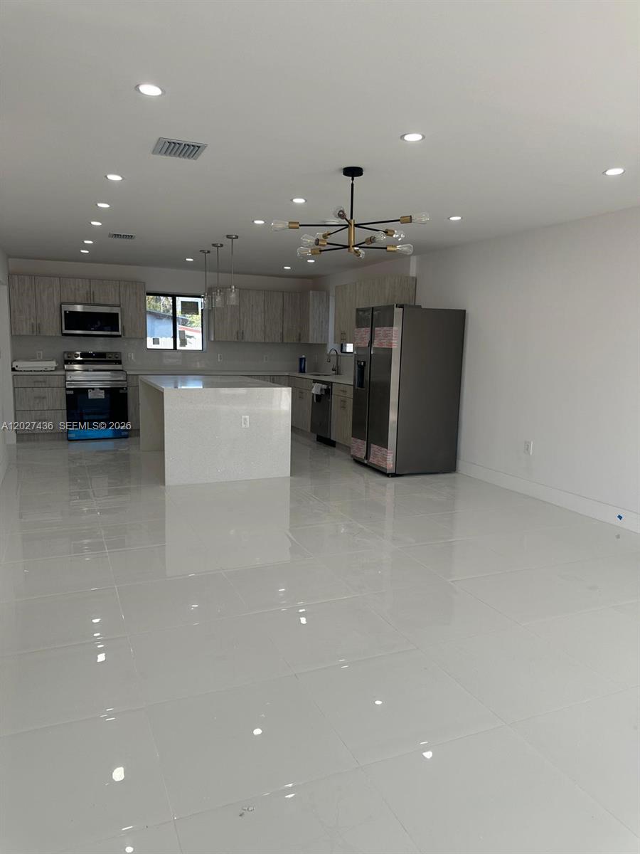 A modern kitchen features white tile floors, light wood cabinets, and a central island — 2041 NW 190th Ter, Miami Gardens FL 33056, MIAMI GARDENS, FL