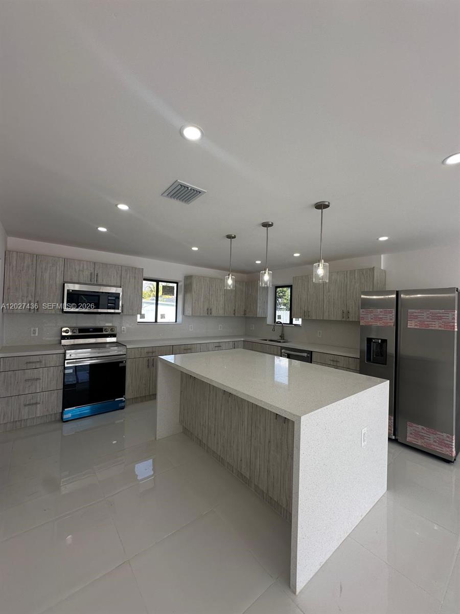 A modern kitchen features light wood-grain cabinets, a white quartz island, and stainless steel appliances — 2041 NW 190th Ter, Miami Gardens FL 33056, MIAMI GARDENS, FL