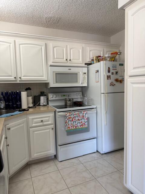 A kitchen features white cabinets, white appliances, and light-colored tile flooring — 812 Sky Pine Way # D2, FL 33415, FL