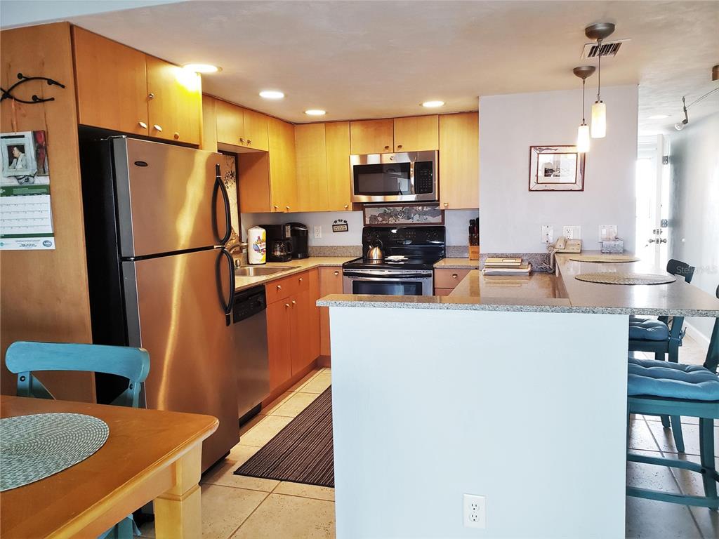 A kitchen features light wood cabinets, stainless steel appliances, and a granite-topped breakfast bar — 4849 SAXON DRIVE UNIT C201, NEW SMYRNA BEACH, FL