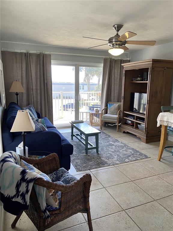 A living room features a blue sofa, wicker chair, wooden entertainment center, and sliding glass doors — 4849 SAXON DRIVE UNIT C201, NEW SMYRNA BEACH, FL