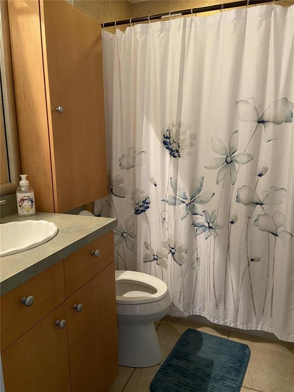 A bathroom features a wood vanity, a white toilet, and a floral shower curtain — 4849 SAXON DRIVE UNIT C201, NEW SMYRNA BEACH, FL