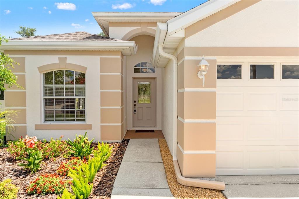 The exterior of a tan house features a front door, a window, and a garage — 2913 BANYAN HILL LANE, LAND O LAKES, FL