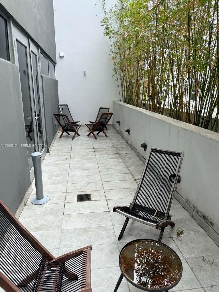 A narrow outdoor patio features light-colored tile flooring, several modern chairs, and a bamboo privacy screen — 538 Meridian Ave, Miami Beach FL 33139, MIAMI BEACH, FL