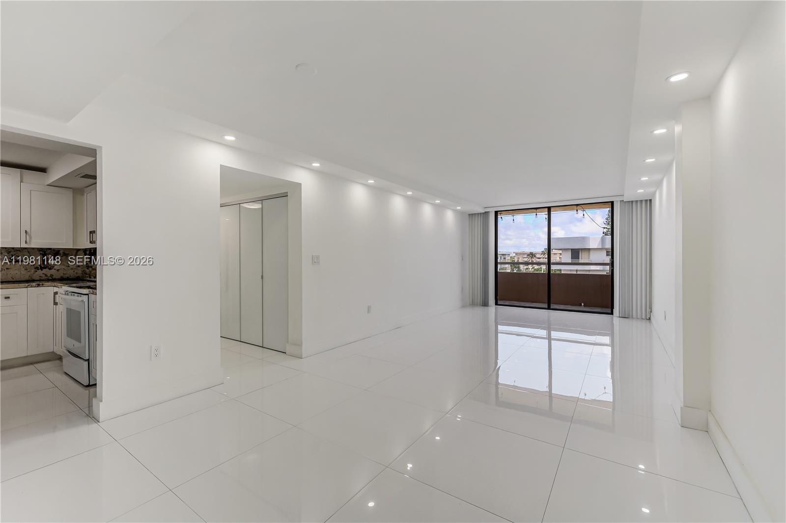 A bright, minimalist living room features white tile flooring, recessed lighting, and a sliding glass door — 8101 Byron Ave # 509, Miami Beach FL 33141, MIAMI BEACH, FL