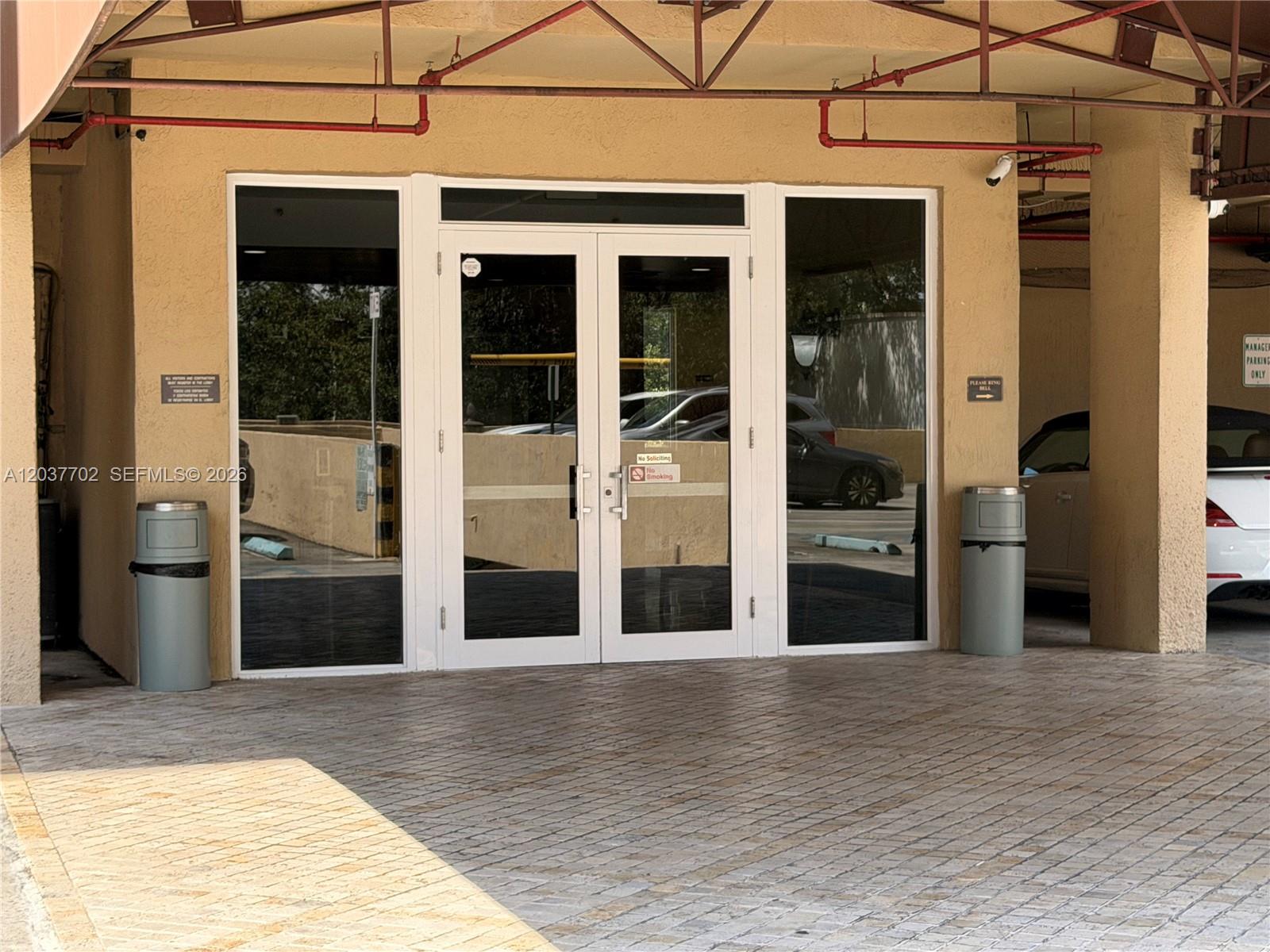 A glass double door entrance with two trash receptacles sits under a covered parking area — 3500 Coral Way # 907, Miami FL 33145, MIAMI, FL