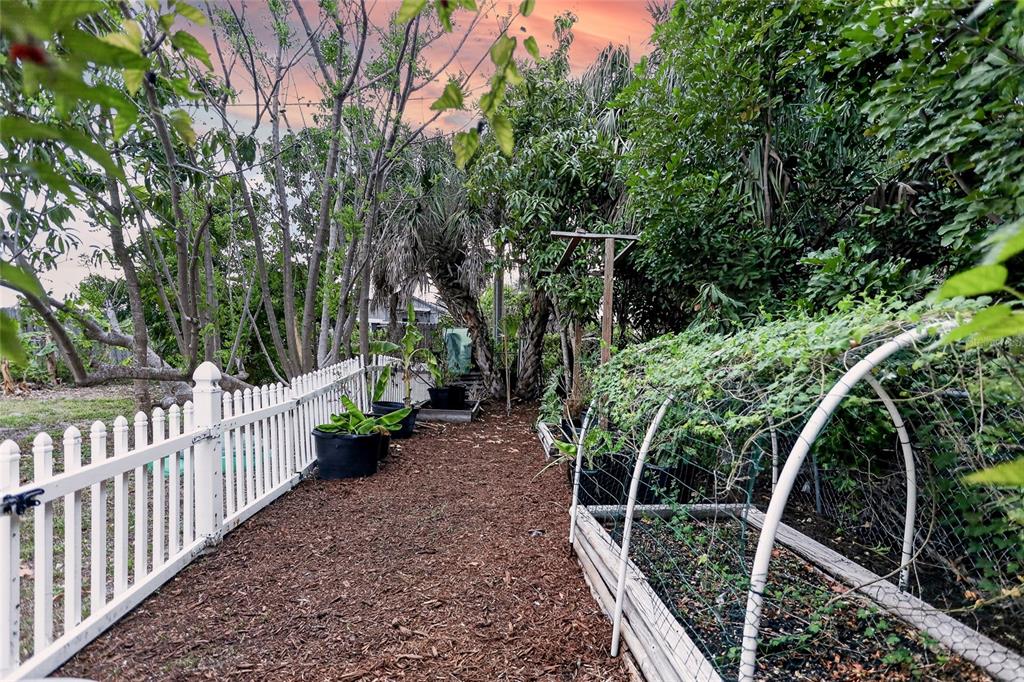 A garden path features a white picket fence, raised planting beds, and various trees — 258 READING STREET NW, PORT CHARLOTTE, FL