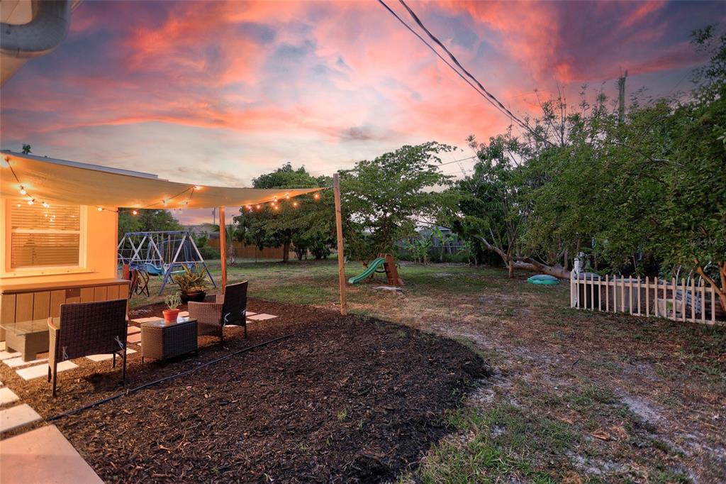 A backyard patio features a shade sail with string lights, outdoor furniture, and a playground set — 258 READING STREET NW, PORT CHARLOTTE, FL