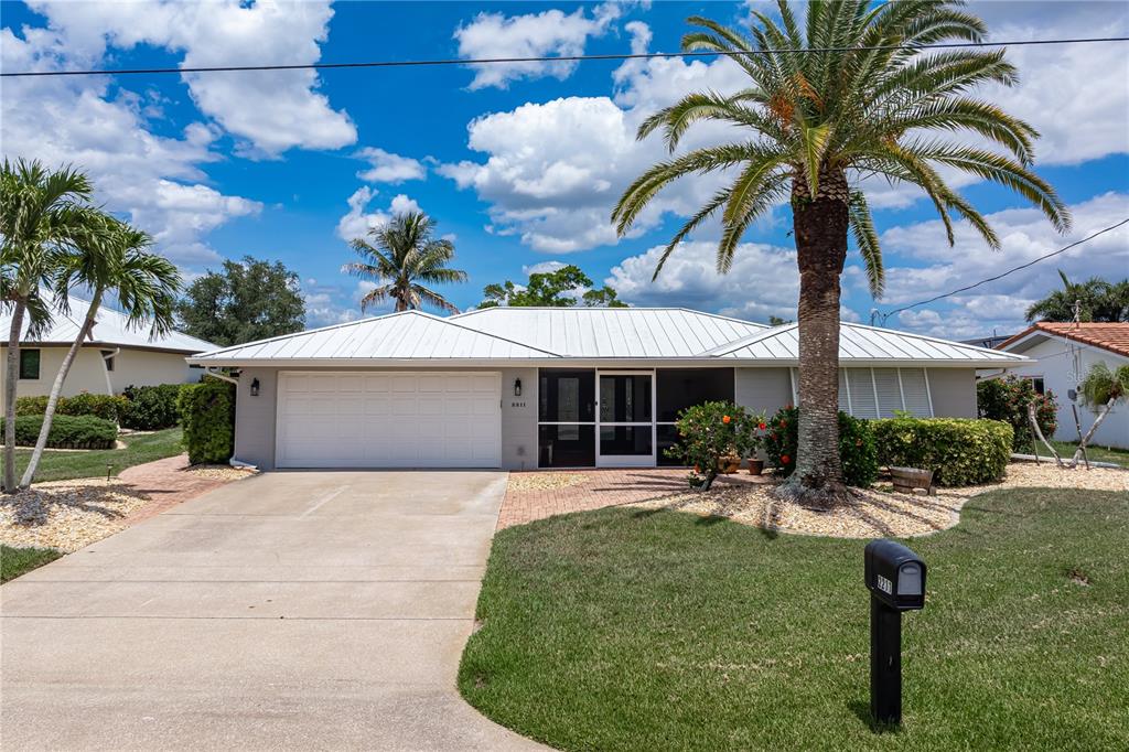 A single-story house with a white metal roof, a two-car garage, and a palm tree — 2211 PALM TREE DRIVE, PUNTA GORDA, FL
