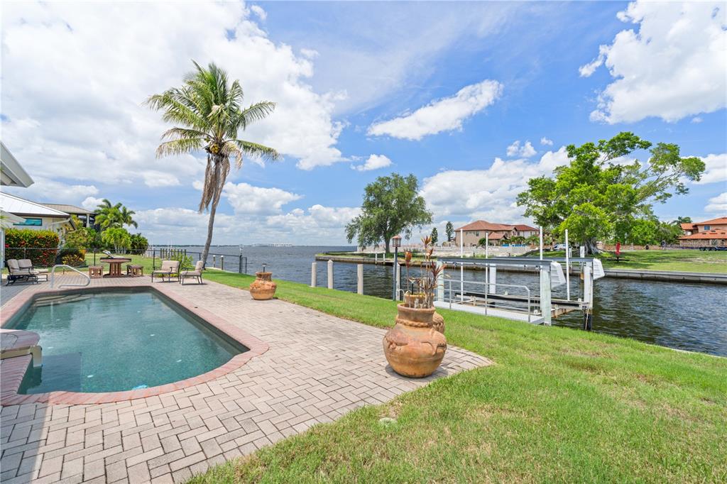 A backyard pool and patio overlook a canal with a private boat lift and dock — 2211 PALM TREE DRIVE, PUNTA GORDA, FL