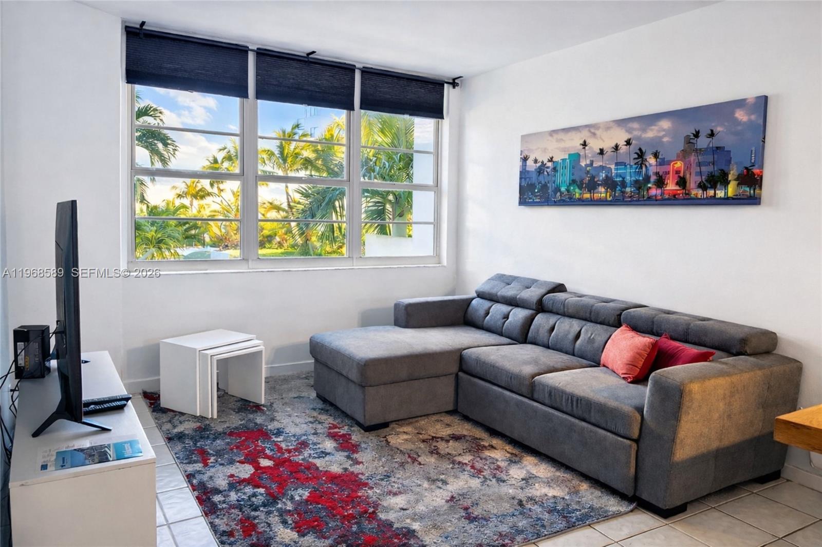 A living room features a gray sectional sofa, a patterned rug, and a large window — 100 Lincoln Rd # 415, Miami Beach FL 33139, MIAMI BEACH, FL